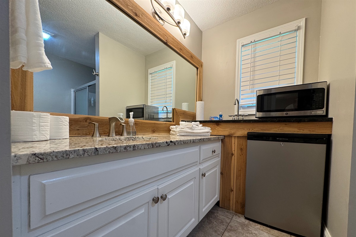 Unique setup with granite vanity and kitchenette area including a sink, fridge, microwave, and storage.