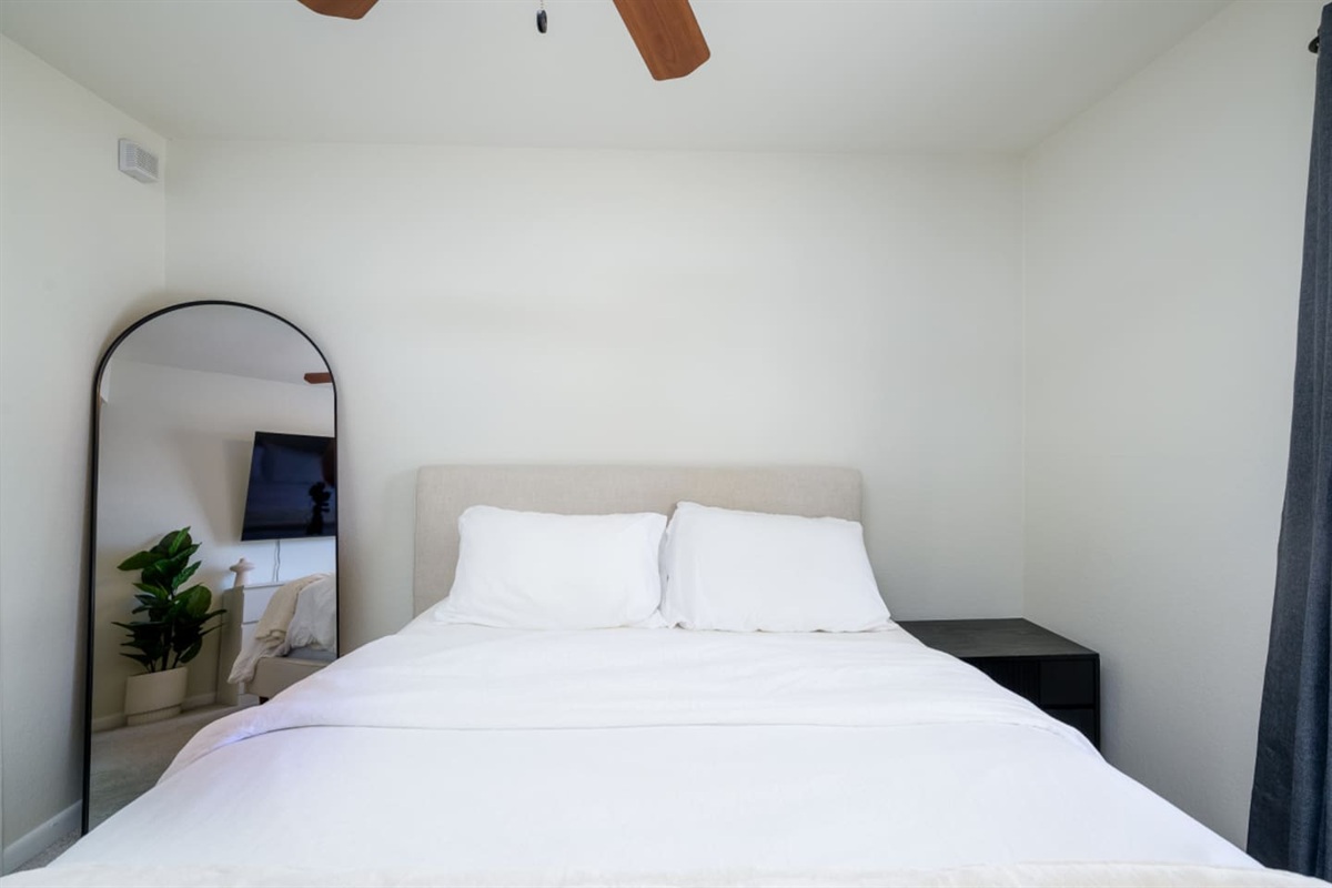 Bedroom with queen bed, wall-mounted TV, ceiling fan, and simple storage for everyday comfort.