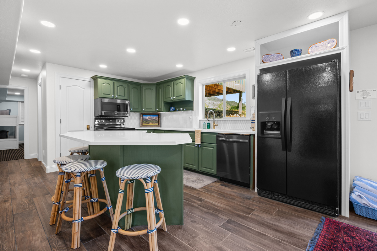 The secondary kitchen features rich green cabinetry, crisp white countertops, full-size appliances, and bar seating for casual dining or morning coffee.