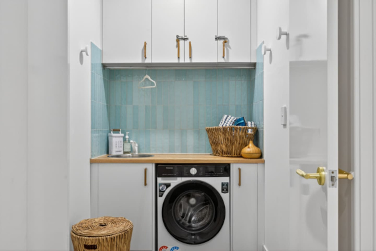 Bright laundry with a front-loading washing machine, tub, hanging rail and baskets, handy for longer stays or sandy beach gear.