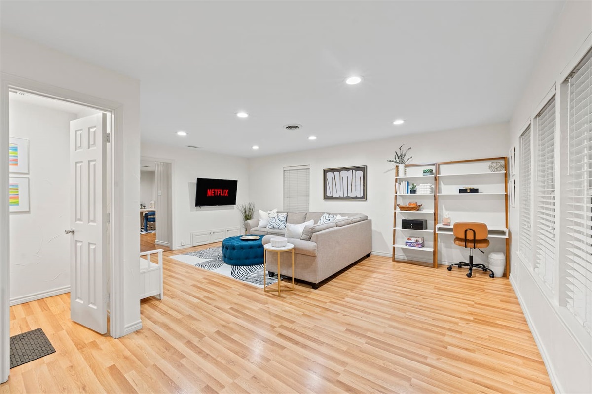 Spacious, light-filled living room with a cozy sectional, smart TV with Netflix, and a dedicated workspace — perfect for relaxing or remote work.
