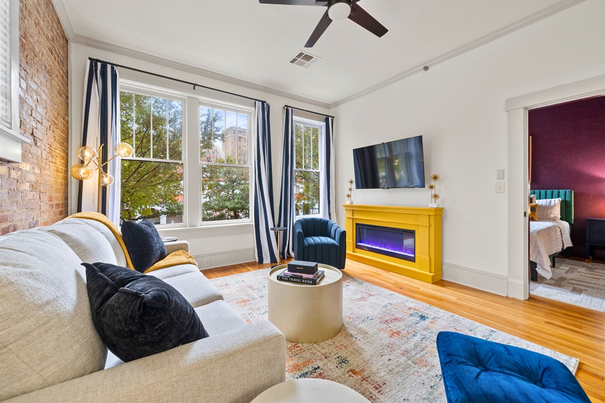 The living area is filled with natural light, colorful accents, and a layout designed for relaxation and entertainment.