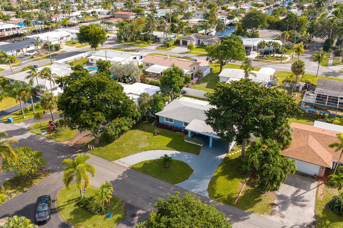 Soaring aerial perspectives highlight the home’s tranquil Pompano Beach neighborhood, private backyard oasis, covered carport, and extended driveway with space for 3 cars.