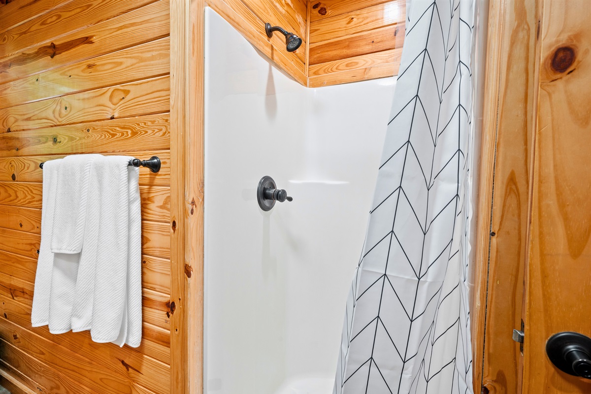 Walk-in shower with clean tile and a patterned curtain adds comfort and simplicity to your stay.