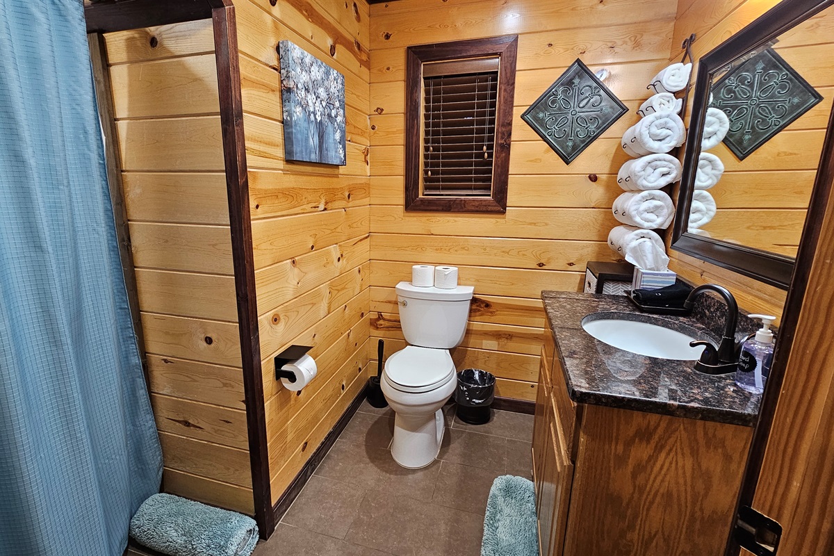 The upstairs ensuite bathroom thoughtfully blends rustic charm with modern amenities, offering a soothing space to get refreshed after a day of exploring Broken Bow.