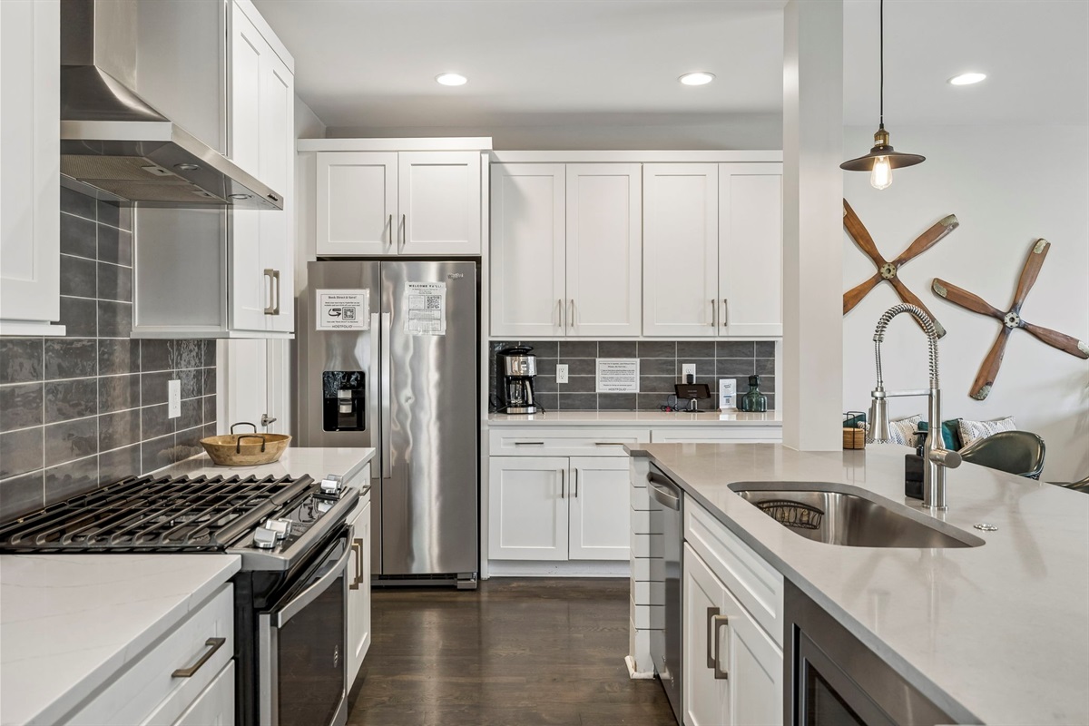 Full gourmet setup with stainless steel appliances, gas range, and large center island - Chic pendant lights, neutral tile backsplash, and extra counter space for easy prep - Wine and snack board welcome you into this stylish, functional culinary space