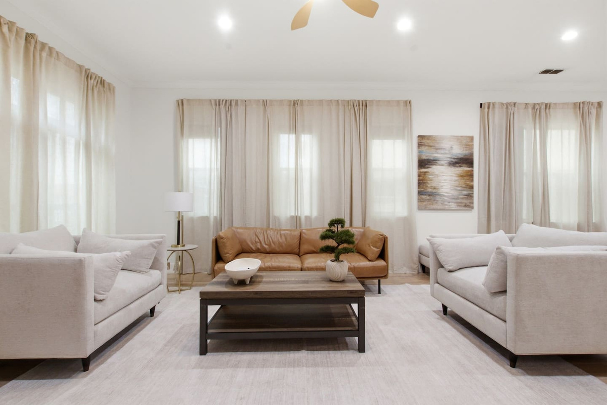 Open-concept living room with ceiling fan, hardwood floors, and natural light from large windows. Comfortable seating for the full group with direct flow to the dining area and kitchen.

