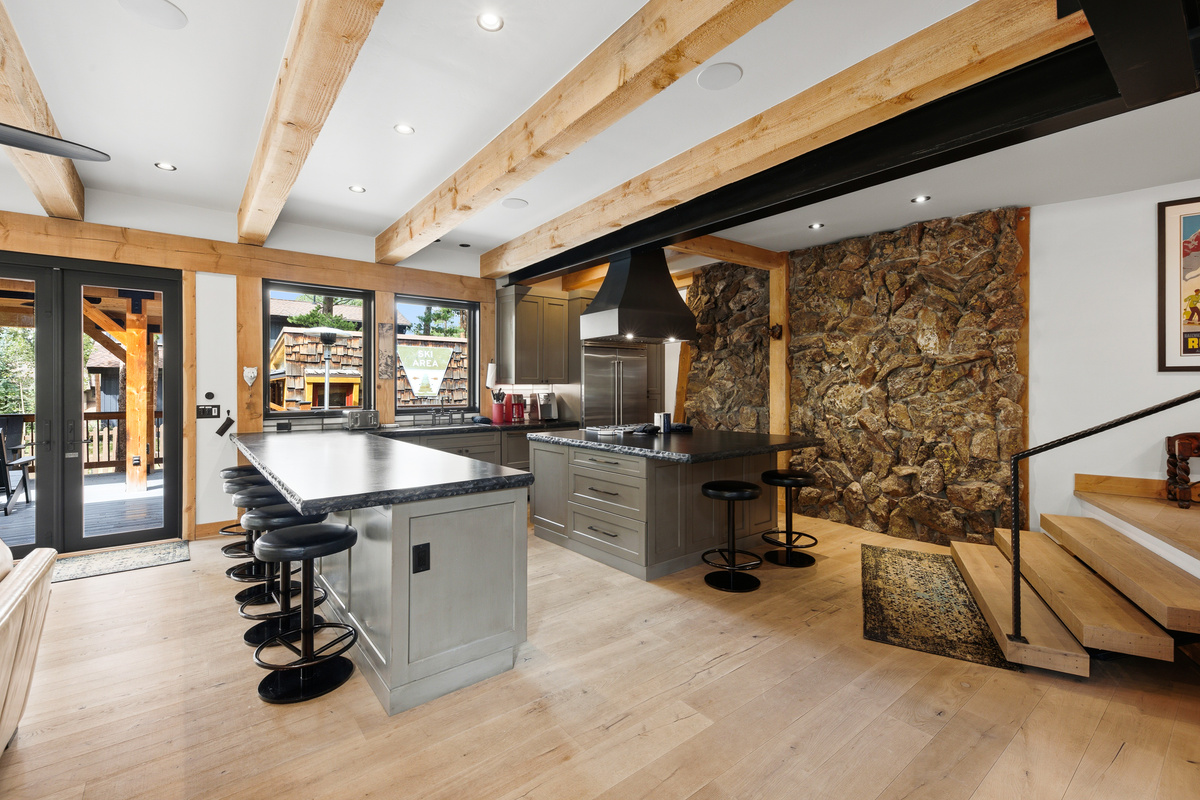 Chef's kitchen with steps to wet bar and entry foyer on right, doors to outdoor living space on left. 
