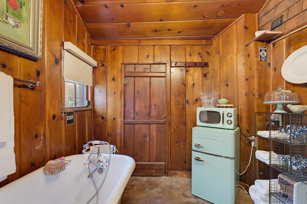 Papaw's Cabin vintage clawfoot soaking tub in knotty pine bathroom with mini fridge, microwave, and rustic 1930s log cabin charm. Cozy Waco Texas vacation rental with modern amenities.