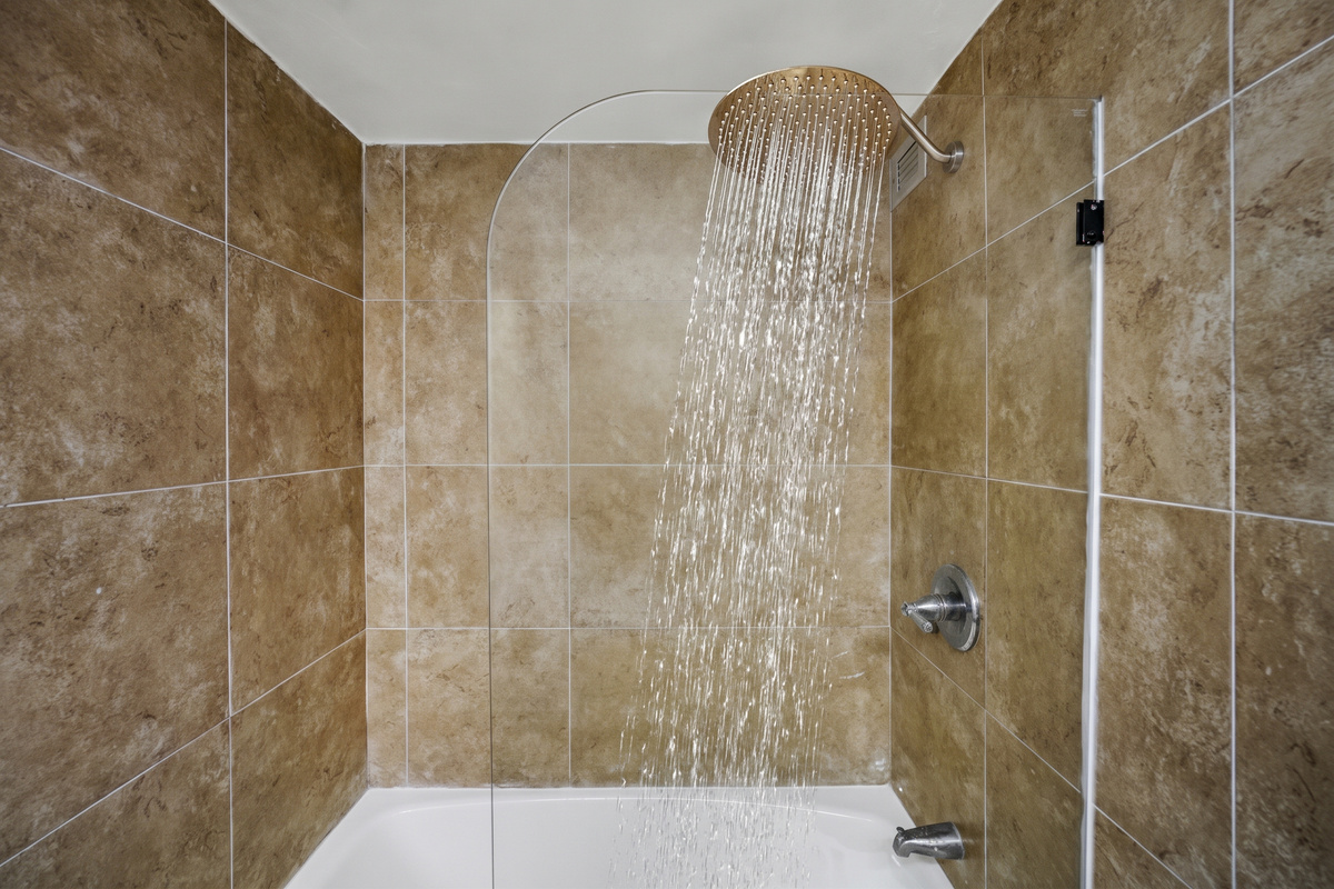 The tub-and-shower combination features a wide stainless steel rainfall shower head behind a frameless glass panel.