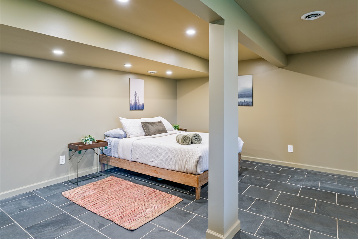 Spacious lower-level queen bedroom with cozy lighting, slate floors, and a clean modern vibe for restful nights.