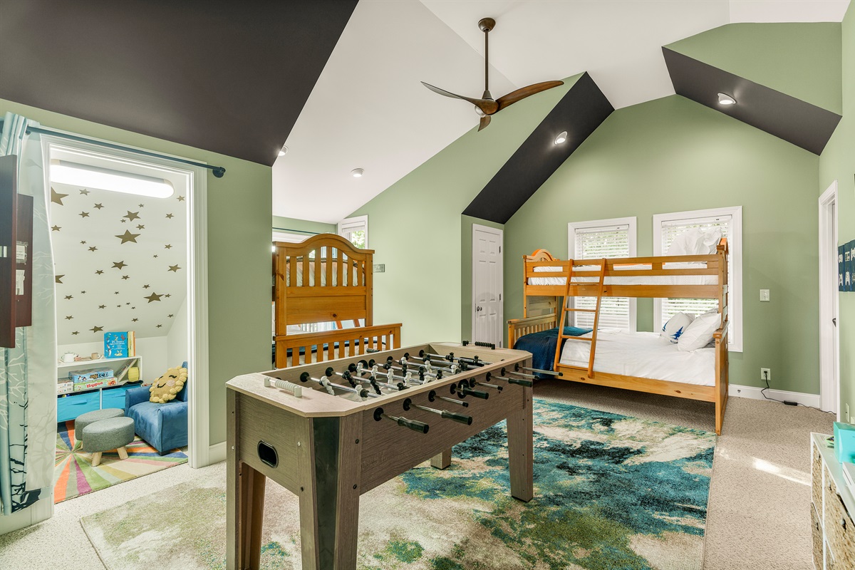 Spacious vaulted bunkroom with two twin-over-full beds, foosball, Xbox, arcade game, safe darts, ensuite bath, and balcony—perfect for relaxing or reconnecting
