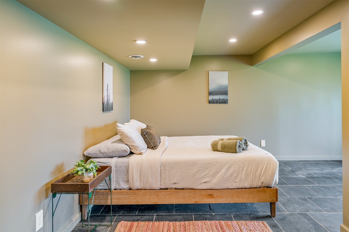 Spacious lower-level queen bedroom with cozy lighting, slate floors, and a clean modern vibe for restful nights.