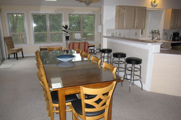 View of the dining table which has 10 chairs and extra seating can be accommodated using the benches in the sunroom.  Three bar stools on the right face the kitchen.  Open floor plan.