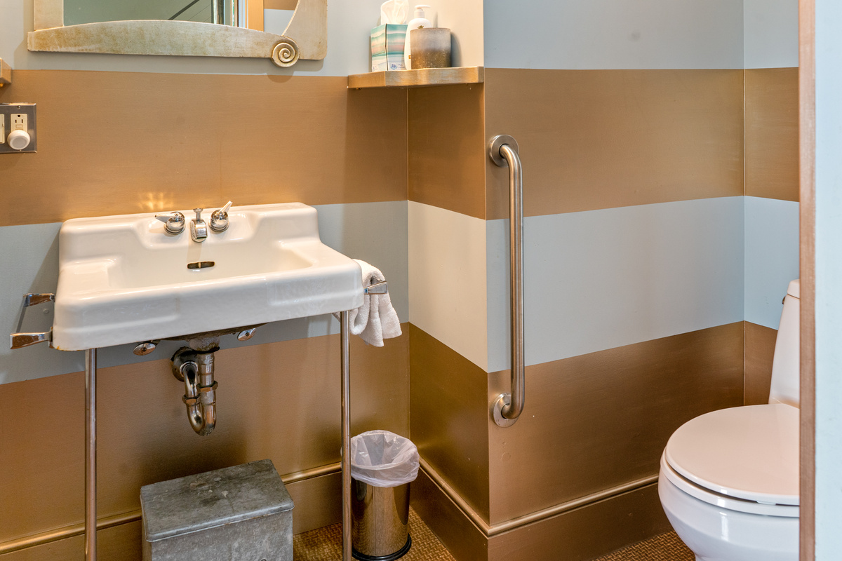 Accessibility meets style in "The Vault" half bath at "The Crag." Features a wall-mounted safety grab bar, open-under console sink, and striking metallic stripes—offering comfortable, stylish ease for all guests.