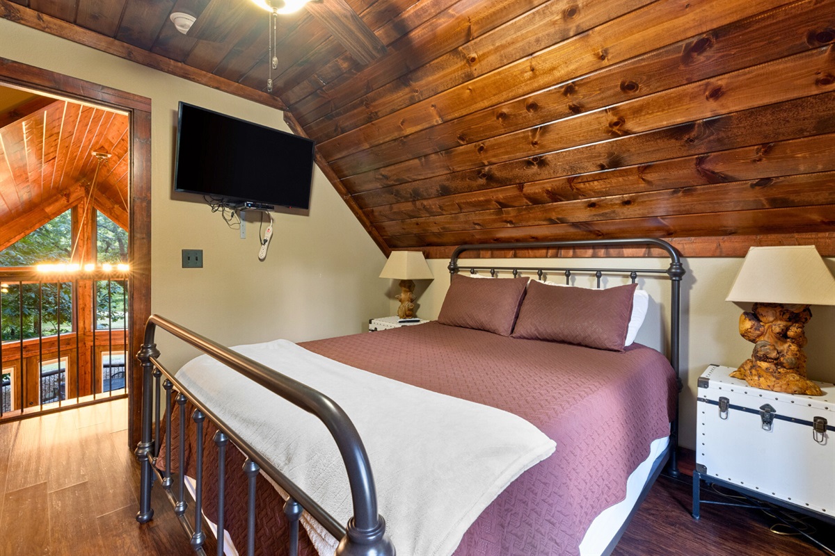 Bedroom 2 coziness—TV, wood ceilings, and warm bedding.