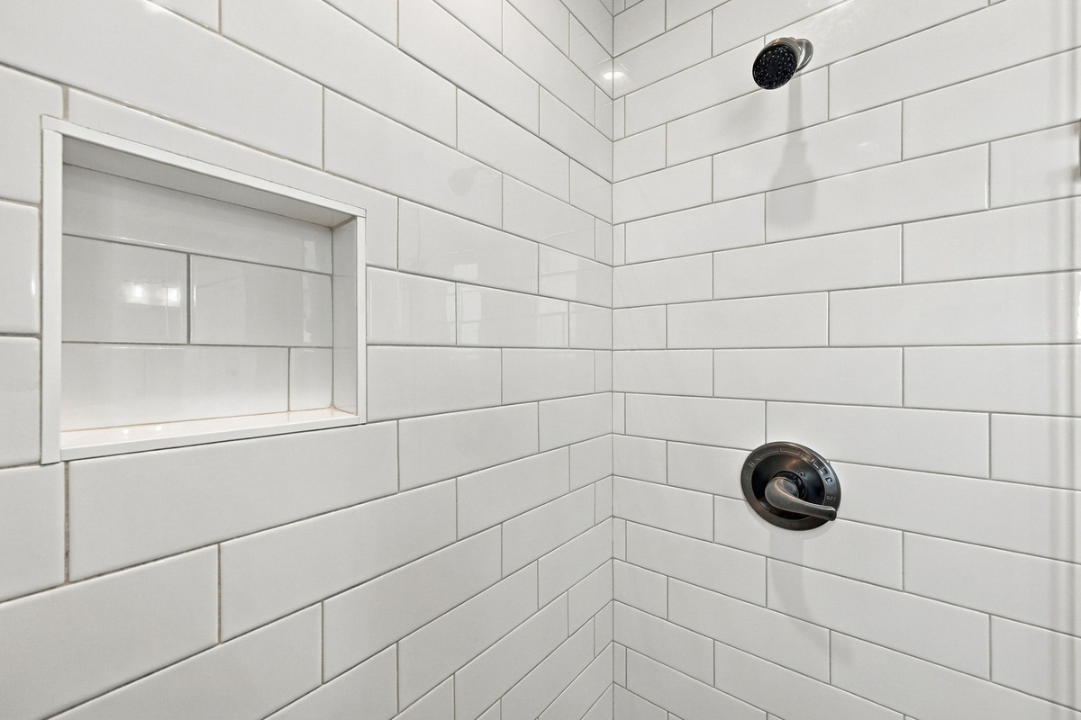 Walk-in shower detail highlighting classic white subway tile, a built-in recessed storage niche, and dark bronze fixtures.