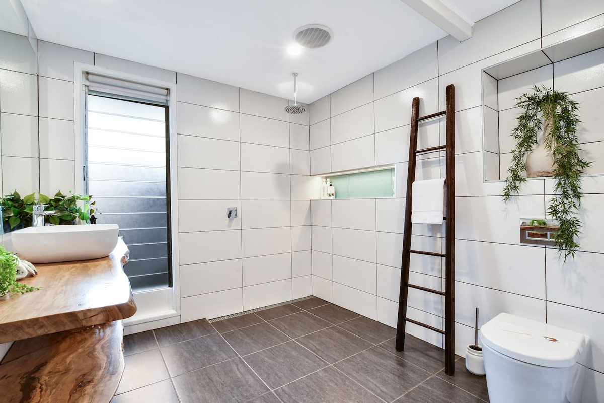 The open shower, natural-edge timber vanity and timber ladder give this bathroom at Aaron's Beachside Boat House a distinctive, character-filled finish.