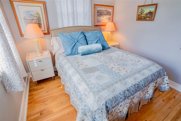 Inviting queen bedroom with natural light, hardwood floors, and soft bedside lamps. Clean, comfortable space for a restful stay.