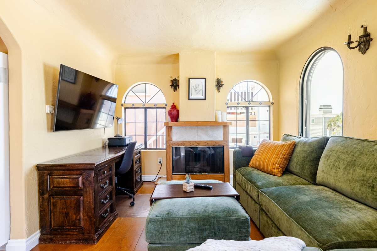 Comfortable Lovesac sectional couch wraps around a gas fireplace and 55" wall mounted TV. Underneath the TV is a laptop workstation with a color printer.