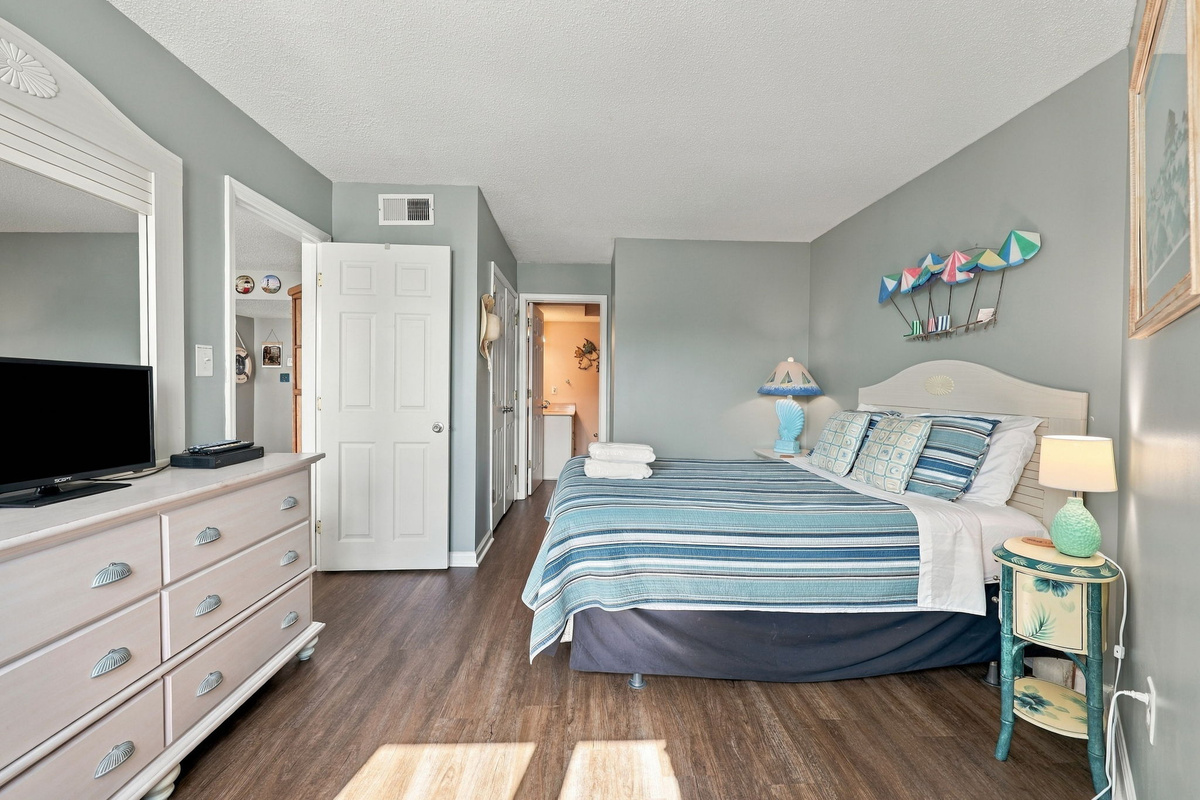 Serene master bedroom featuring a white wooden dresser, matching nightstand, and a queen bed with blue coastal bedding.
