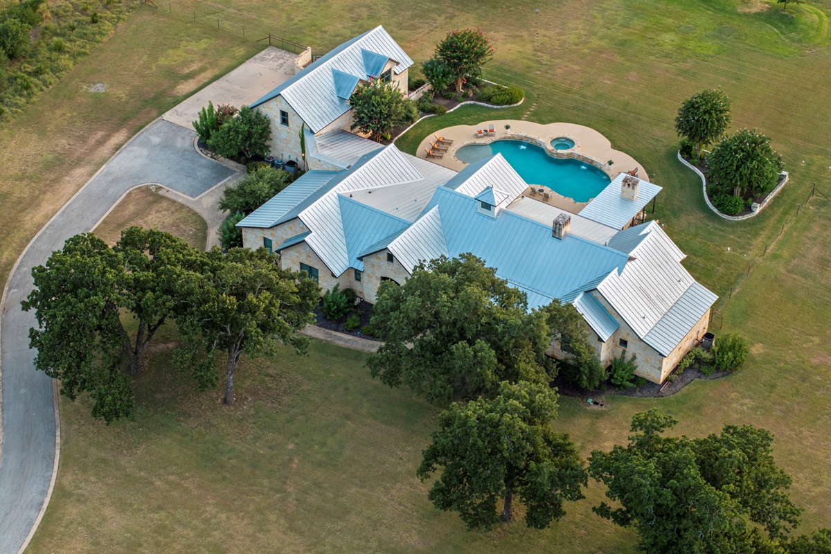 Bird's-eye perspective of a beautiful home and its expansive grounds, featuring a sparkling swimming pool and hot tub.