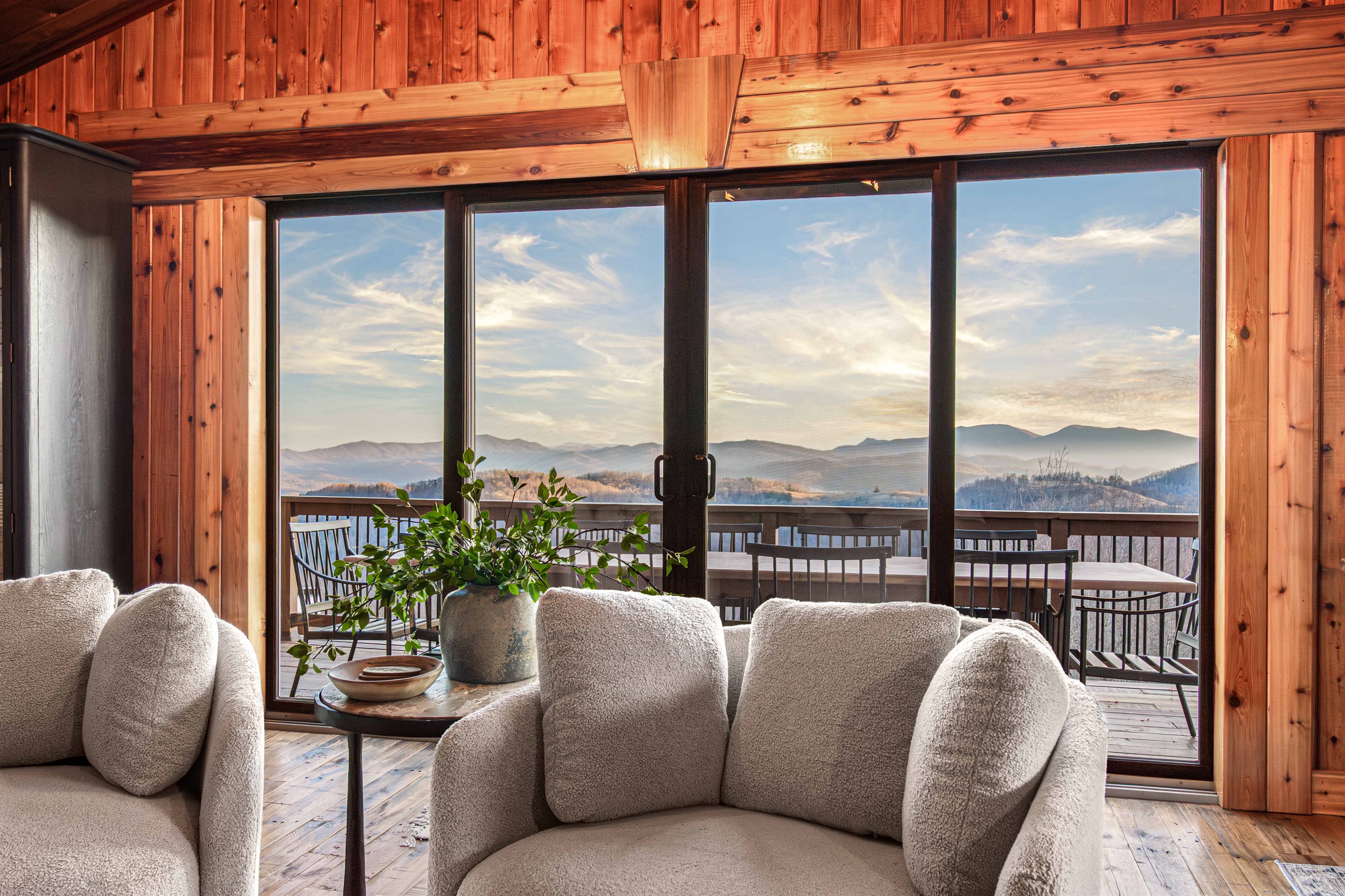 Cozy living space on the "old side" of the house with floor-to-ceiling windows, large cozy chairs in front of a wood burning fireplace and direct access to the deck and breathtaking mountain views.