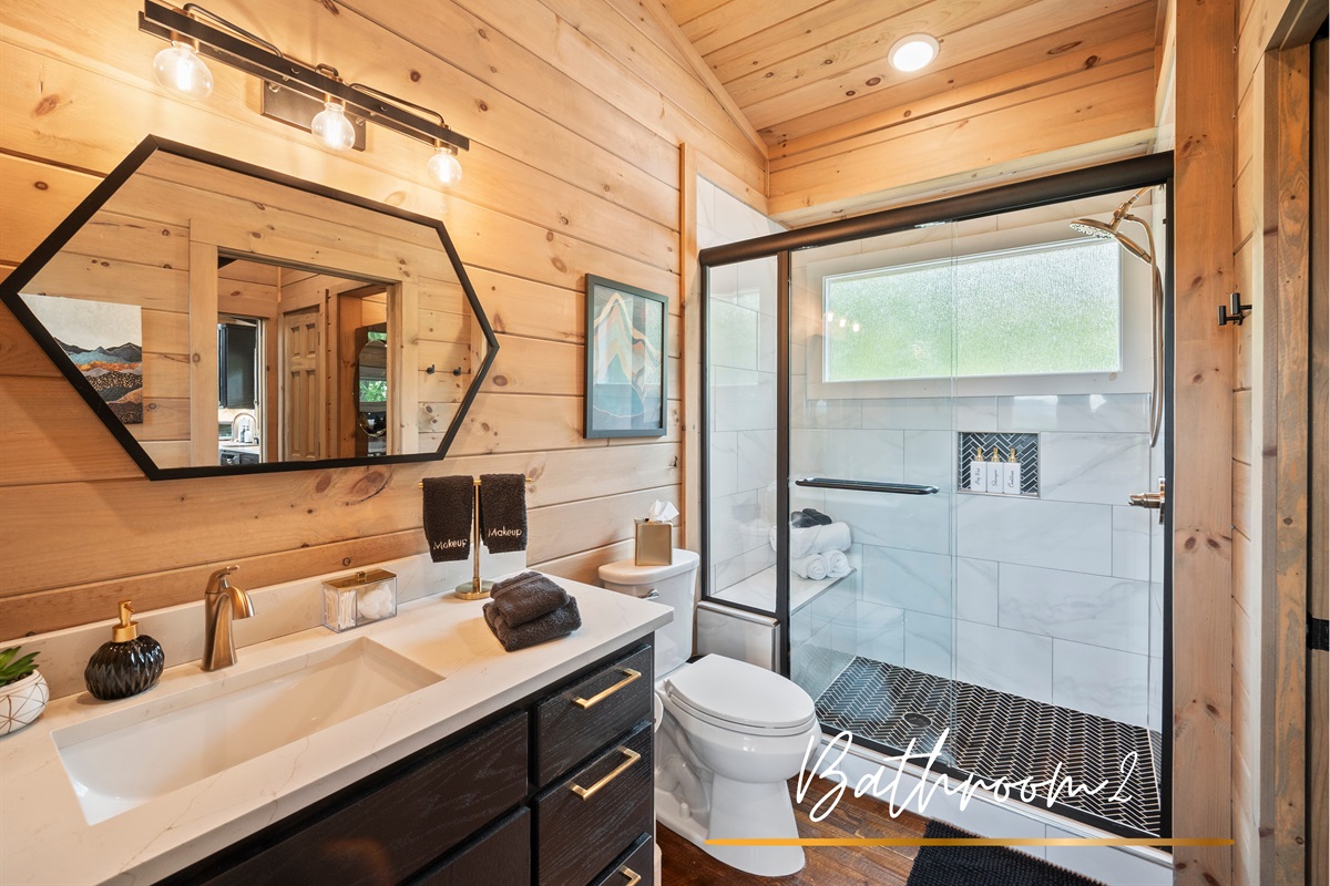 Bathroom-two features a walk-in shower with modern black and gold accents. Chic, functional, and effortlessly stylish.