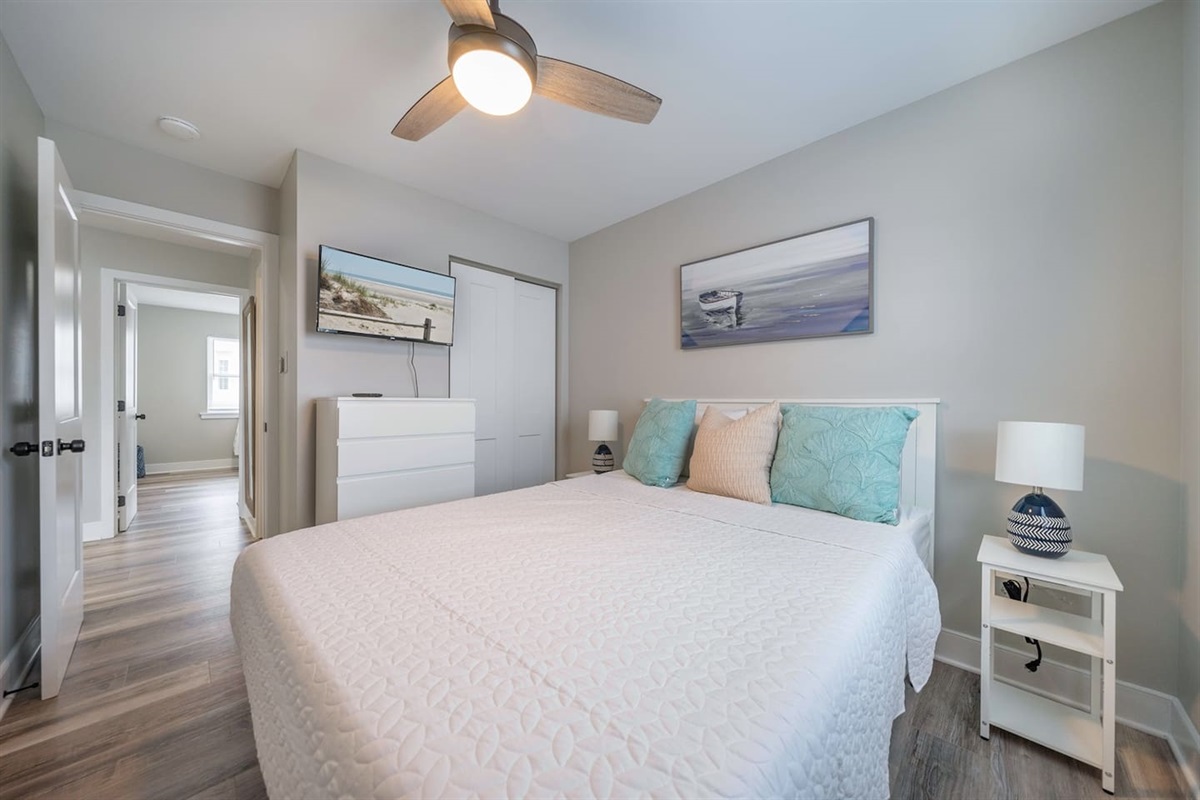 Calm and comfortable bedroom featuring a plush king bed, soft coastal tones, and ceiling fan for added comfort. Includes a dresser, closet storage, and wall mounted TV, offering a restful space to unwind after a full day out.