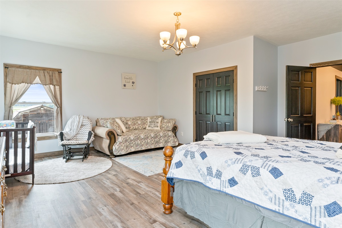 Inviting master Queen room with a comfy queen fold out sofa, crib, and rocking chair—ideal for families. Natural light fills the space, creating a warm and welcoming retreat. Bedroom #1