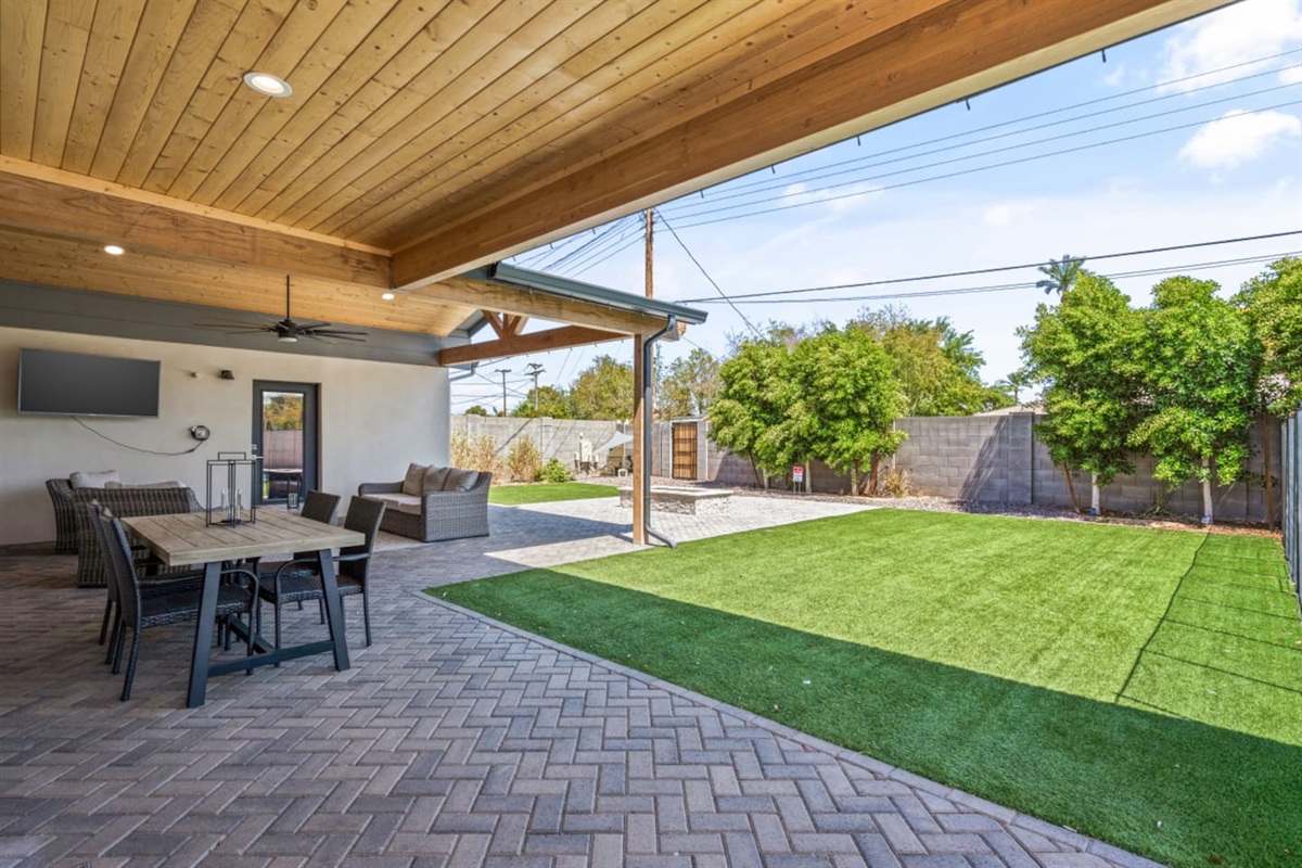 Outdoor living area with shaded lounge space, fire pit, and a clear view toward the pool.