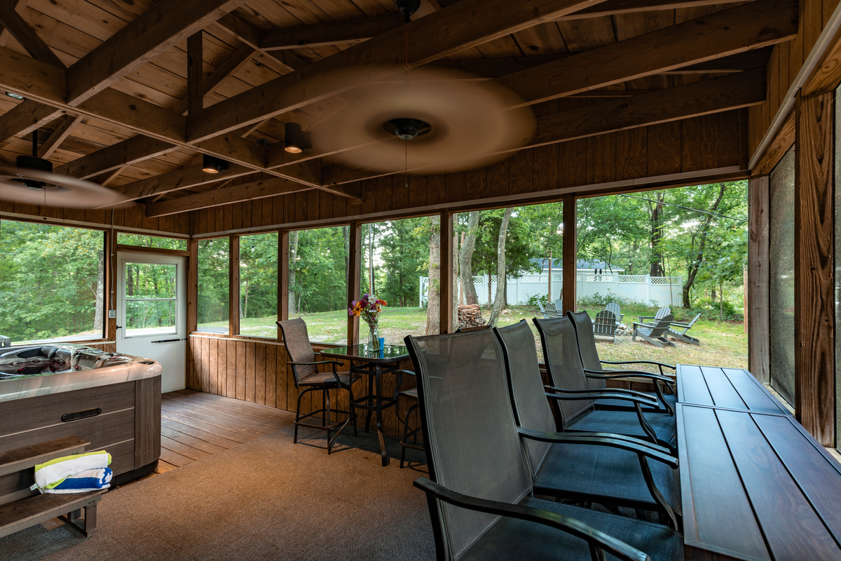 The screened porch brings everyone together with a hot tub, dining space, and peaceful woodland views—without the bugs.