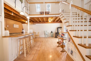 An open dining area in the back, decorated with a mix of vintage-style chairs and a wood-burning stove in the corner, enhancing the homely atmosphere.