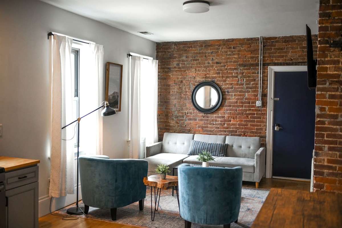 Bathed in natural light, this vibrant space offers a stylish L-shaped sofa, a sleek coffee table, and a cozy setup that blends comfort with modern charm.