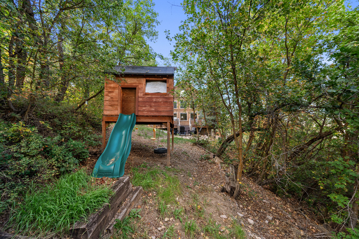 Children’s playhouse and slide surrounded by trees for outdoor family fun.