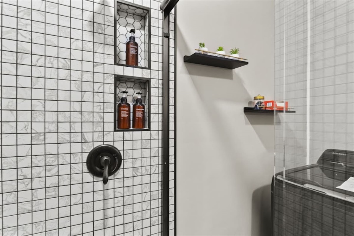 Modern full bathroom featuring a glass-covered shower, elegant walling, a shower heater, and neatly arranged shampoo and body wash—designed for functionality and relaxation with a touch of sophisticated style