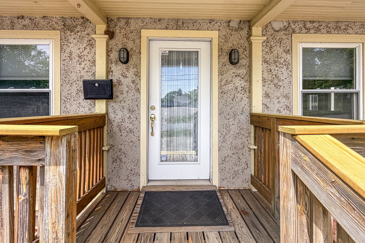 The covered porch deck provides a close-up look at the unique stone-pressed stucco siding and outdoor lighting. While this door forms the classic facade, the active keyless entry pad for guest check-in is located at the side mudroom door.