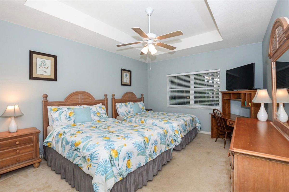 Comfortable bedroom featuring a large bed, ceiling fan, dresser storage, TV, and natural light.