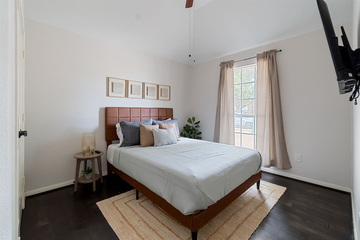 Welcome to our tranquil bedroom featuring a queen bed, softly illuminated by a side table lamp, with sunlight streaming through the window.