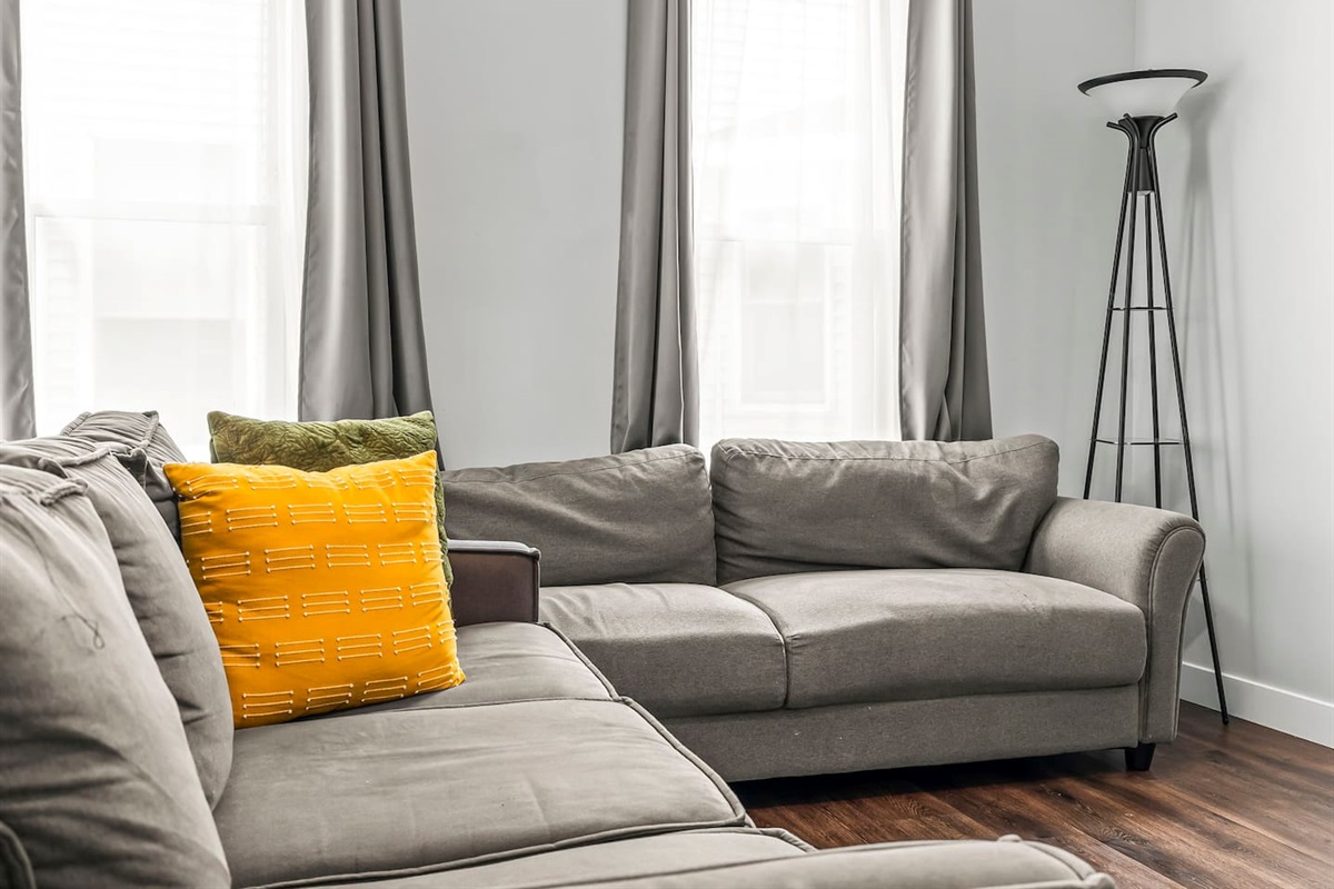 Close-up view of the plush sectional sofa with cozy accent pillows and natural light pouring in from tall windows.