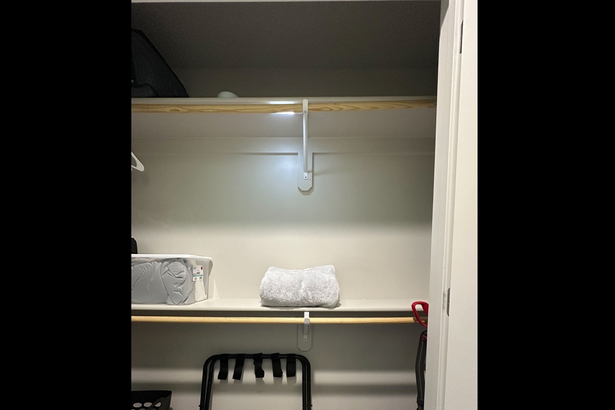 Generous primary closet stocked with extra linens and blankets, plus luggage rack, laundry basket, and vacuum for convenient extended stays.