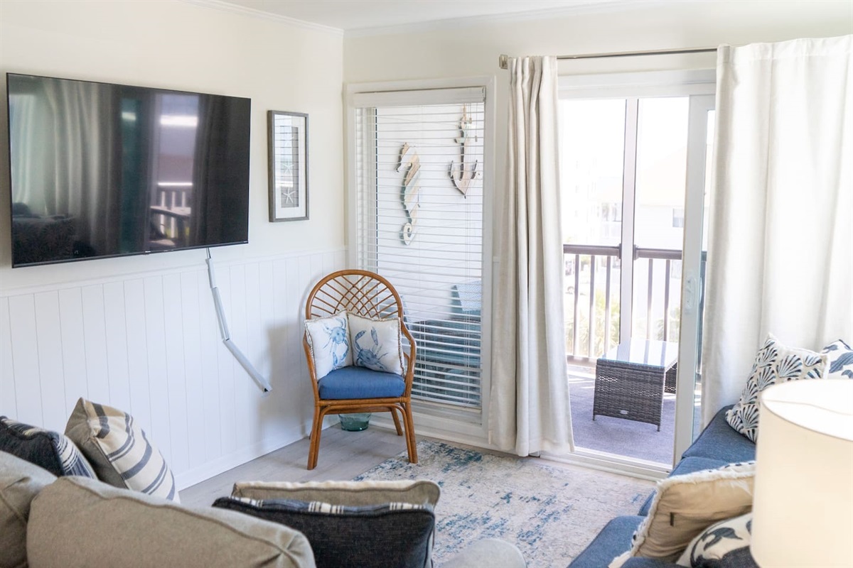 A charming rattan chair, ocean-inspired pillows, and seaside décor create a calming escape, while the private balcony beckons just beyond.
