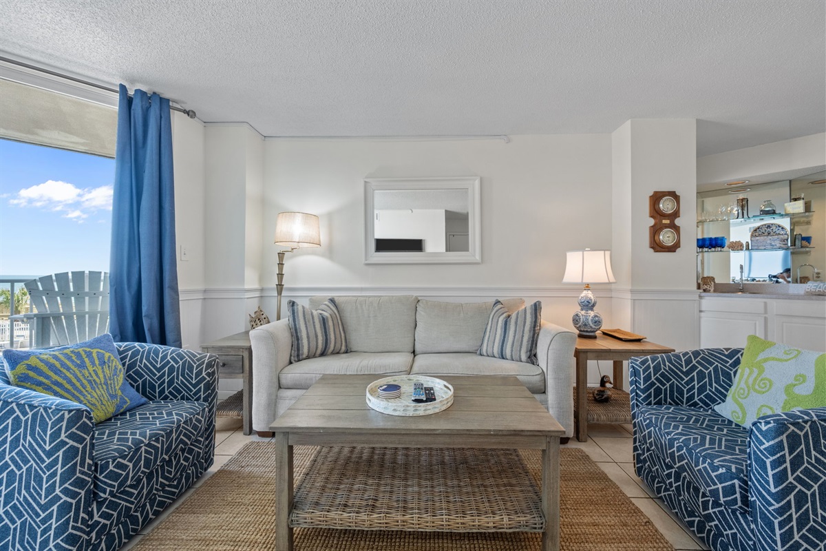Bright coastal living room with comfortable seating, smart TV, and balcony access for indoor-outdoor relaxation
