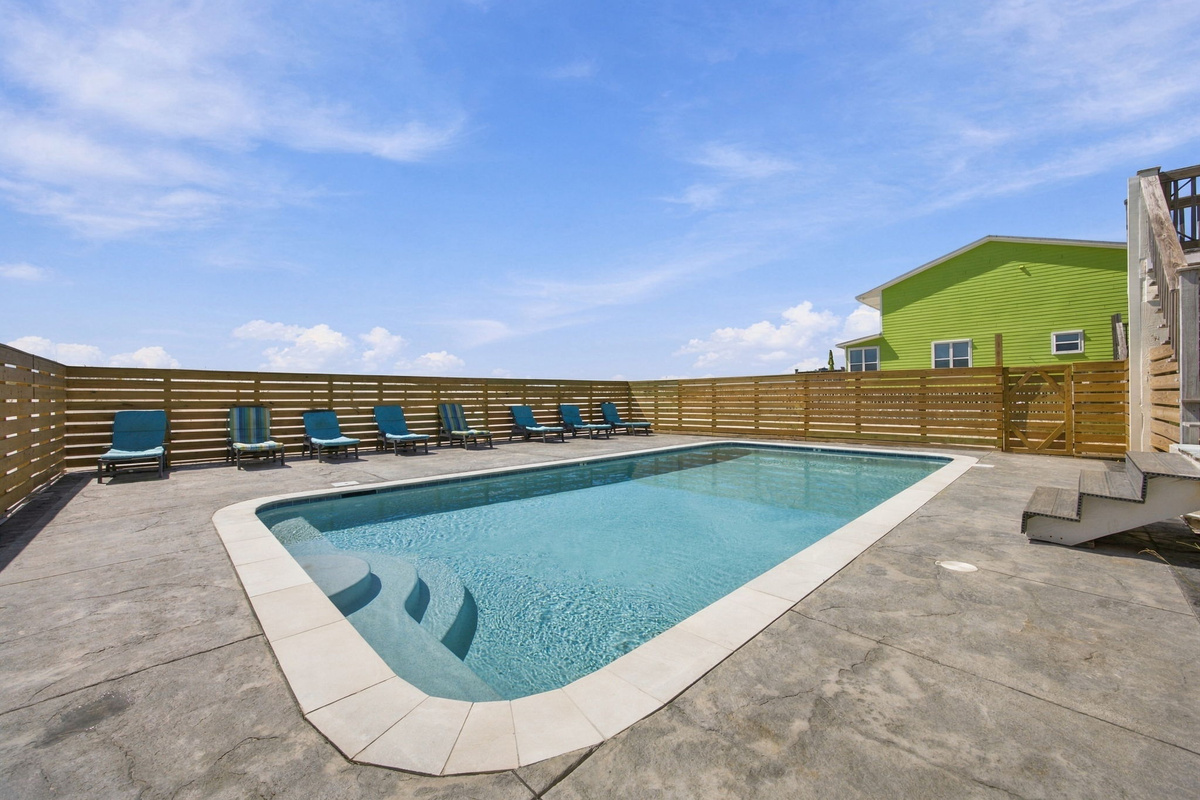 Shared swimming pool with lounge chairs and a spacious pool deck, offering a relaxing place to enjoy sunny beach vacation days.