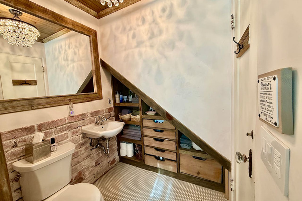 Drawers and shelves tucked beneath the stairs keep towels and complimentary toiletries close at hand, while the chandelier casts playful patterns across the bathroom walls.