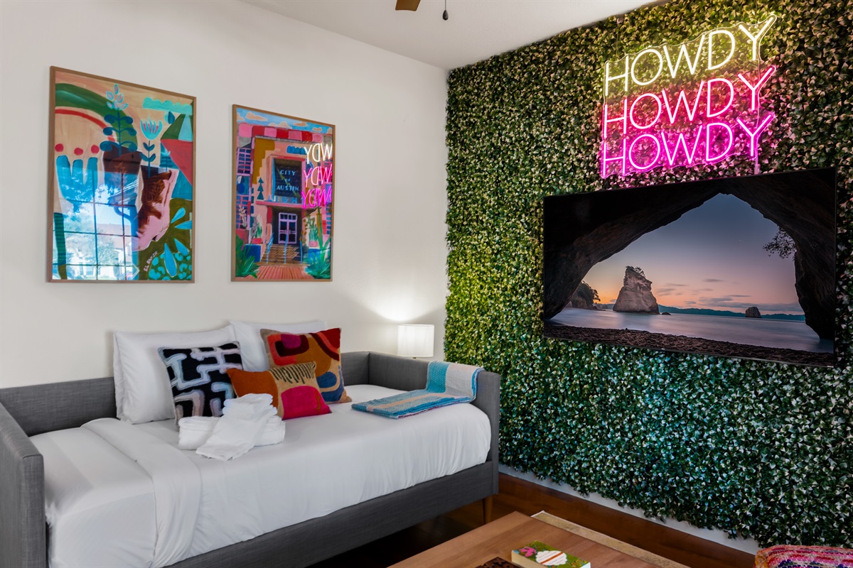 Cozy corner adjacent to dining, adorned with a warm "HOWDY" neon sign, featuring a comfortable twin-day bed.