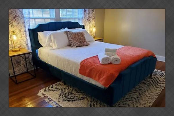 Bright and cozy bedroom featuring a stylish upholstered bed, vibrant decor, fresh towels, and natural light—ideal for relaxing and unwinding.