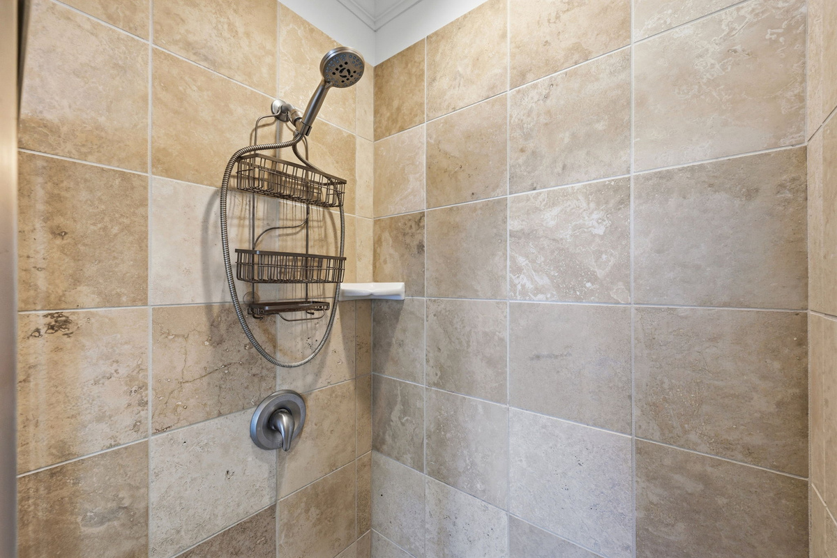 Walk-in tiled shower with built-in corner shelf and modern fixtures in a clean coastal design