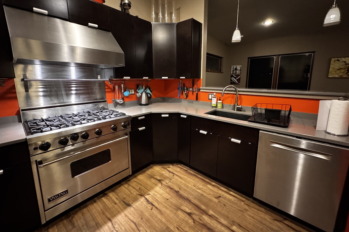 Functional kitchen layout featuring a stainless steel dishwasher and deep sink. The open pass-through looks directly into the dining area, keeping the group connected between meal prep and dinner at this modern Acadia retreat.