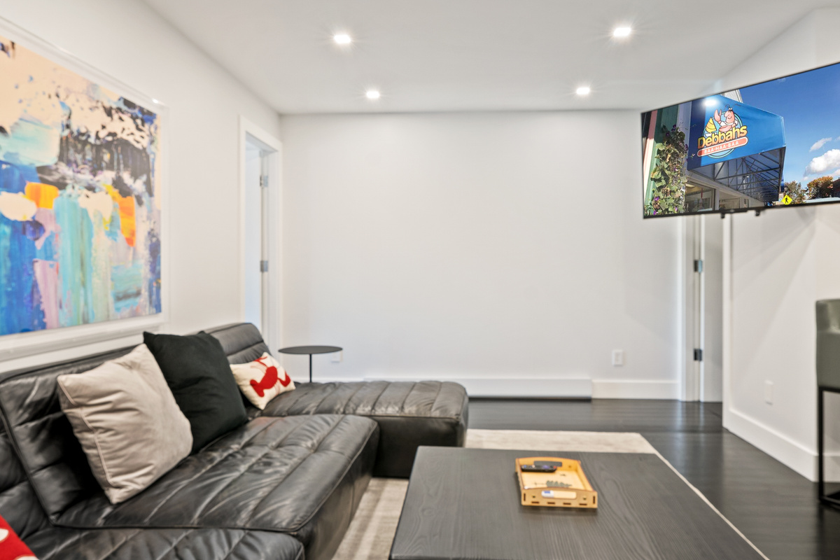 View from the bunk room doorway showing the open-concept design. Relax on the black leather sectional and watch the 55-inch Roku smart TV after a day exploring Acadia National Park. Located right in the heart of downtown Bar Harbor.